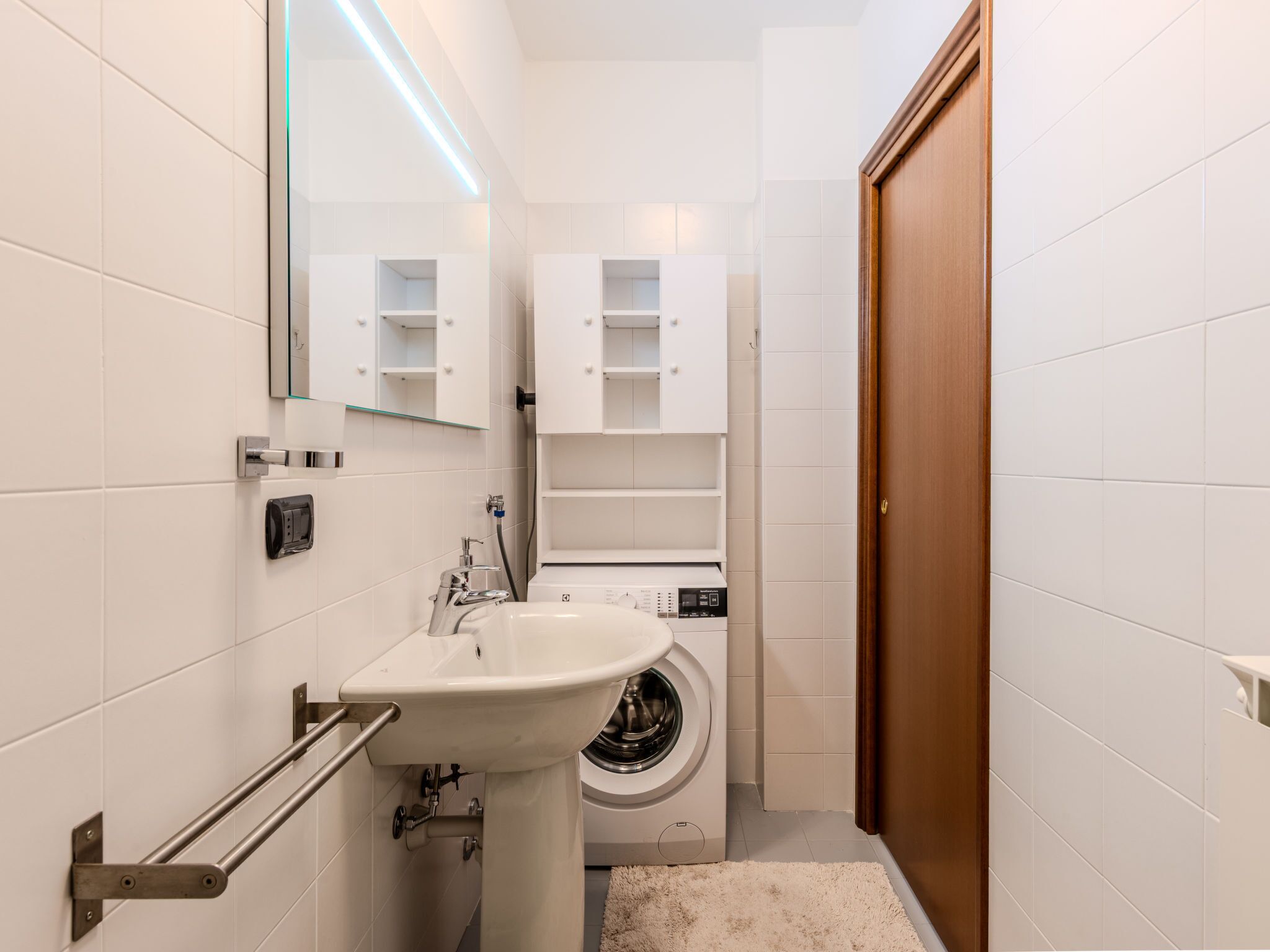 A compact bathroom with a sink, mirror, and a washing machine.
