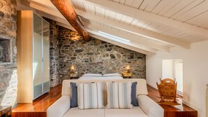 Un dormitorio acogedor con pared de piedra, viga de madera en el techo, sofá blanco y una silla de madera.