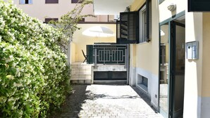 A courtyard with a paved walkway, a green hedge, and a building with a black gate and windows. - Casa Lido mare by Interhome (Lido di Camaiore)