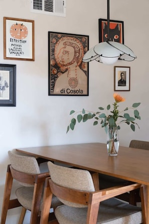 Ein Essbereich mit einem Holztisch, zwei gepolsterten Stühlen, einer Vase mit Blumen und gerahmten Kunstwerken an der Wand.