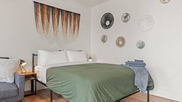 A bedroom with a bed, a nightstand, a lamp, a chair, and decorative wall art.