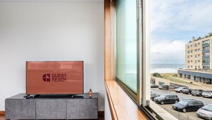A modern hotel room with a large window offering a view of the ocean and a parking area. - GuestReady - Serene hideout in Leça da Palmeira (Porto)