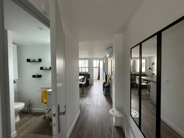 Un appartement moderne doté d’un couloir central qui donne accès à un espace de vie, une cuisine et une salle de bain.