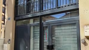 A building with a black metal facade, a double door with a glass panel, and a sign indicating a tattoo parlor.