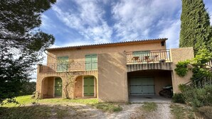 Una casa a due piani con vialetto sterrato, persiane verdi e un balcone con ringhiera.