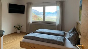 A bedroom with a bed, a TV, a window with curtains, a radiator, and a potted plant. - Farm with small animals, beautiful and quiet location, with panoramic view (Latsch - Tarsch)
