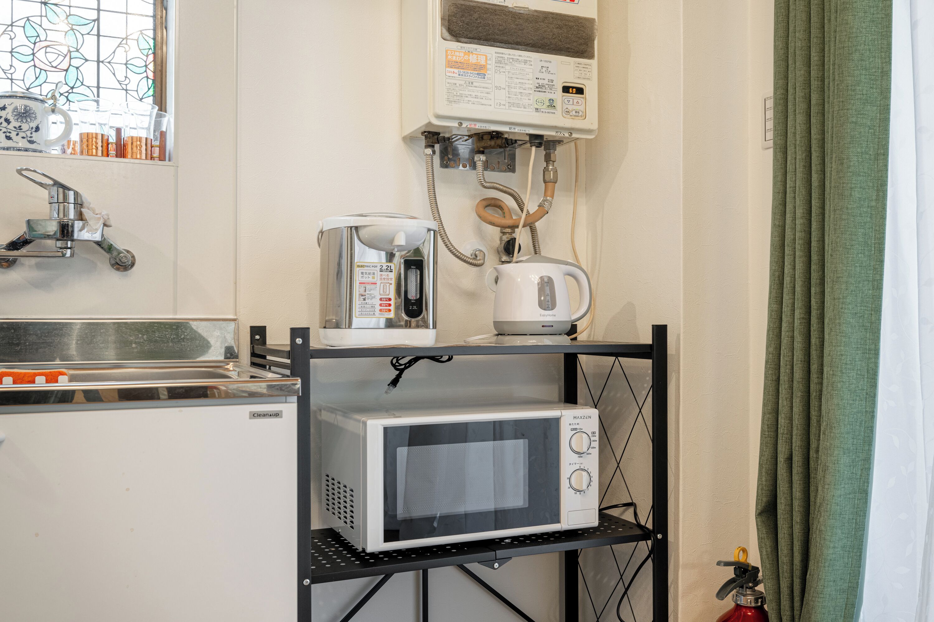 Une cuisine compacte équipée d’un micro-ondes, d’un grille-pain et d’une bouilloire placés sur une étagère, d’un évier et d’une fenêtre ornée de vitraux.