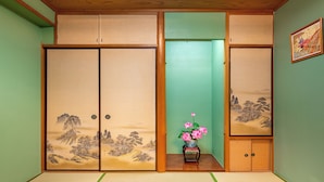 A traditional Japanese room with tatami flooring, sliding doors with landscape paintings, and a vase with pink flowers. - Asakusa Temple 4min Skytree 10min Japanese Cozy House  (Tokyo)