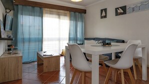 Un comedor con una mesa redonda y cuatro sillas blancas, una mesita auxiliar y un sofá.