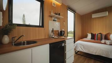 A modern kitchen with a built-in dishwasher, a window with a view of trees, and a bed with multiple pillows and a blanket.