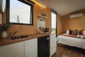 A modern kitchen with a built-in dishwasher, a window with a view of trees, and a bed with multiple pillows and a blanket.