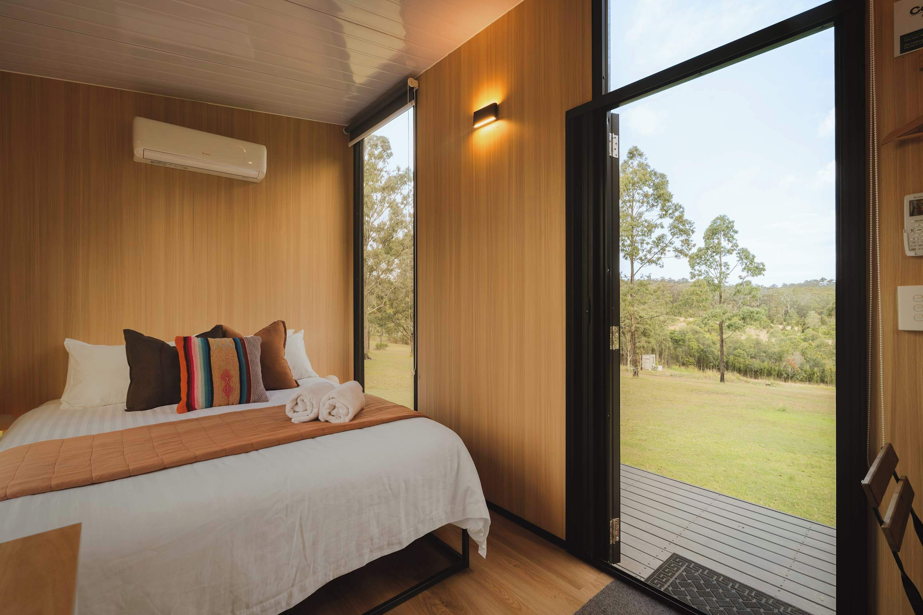 A bedroom with a large bed, wooden walls, a window, and a view of the outdoors.