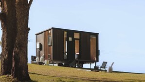 A small, wooden cabin with a flat roof, situated on a grassy hill with a clear sky.