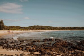 Una playa con costa rocosa, agua cristalina y una extensión de arena.