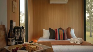 A hotel room with a bed, a bedside table with a bottle, glasses, and a plate of food.