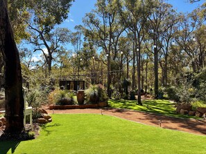 A well-maintained garden with a variety of plants and trees, a clear sky, and a small structure in the background. - Jarrah Valley "Sunset" by Tiny Away (Bedfordale)
