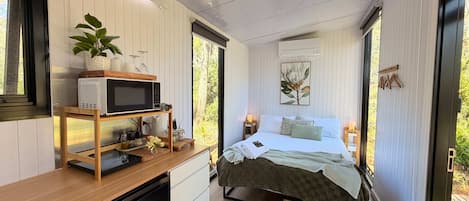 Un dormitorio compacto con cama, mesitas de noche, microondas y una pequeña zona de kitchenette.