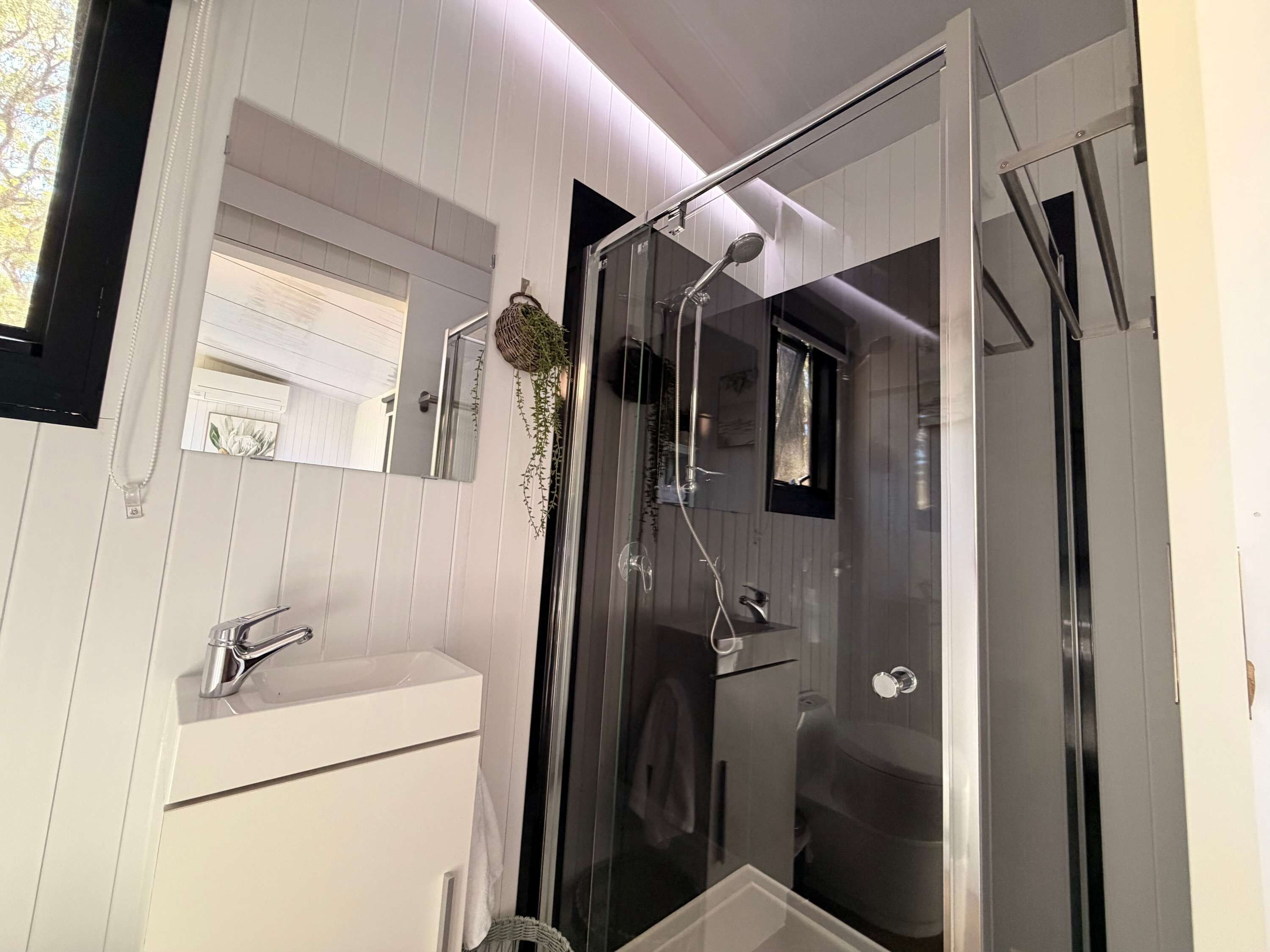 A modern bathroom with a glass shower enclosure, a white sink, and a mirror.