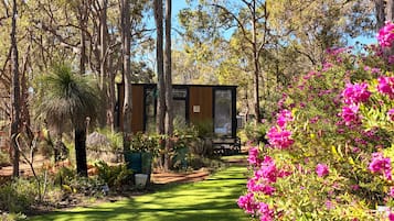 A garden with a pathway leading to a wooden structure, surrounded by trees and flowering plants.