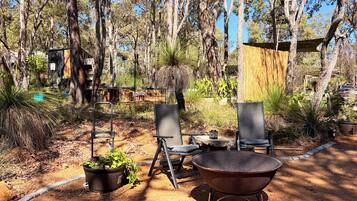 An outdoor seating area with chairs and a fire pit, surrounded by trees and a fenced enclosure.