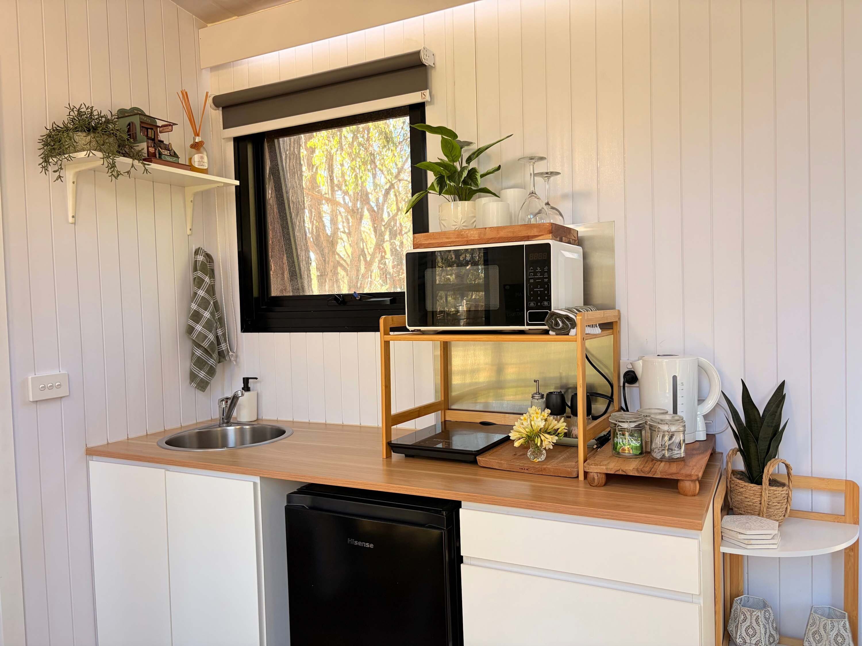 Une cuisine compacte équipée d’un lave-vaisselle encastré, d’un four à micro-ondes posé sur un meuble en bois, d’un évier et d’une fenêtre donnant sur les arbres.