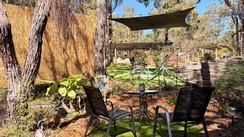 Un área de estar al aire libre con una mesa y sillas, rodeada de árboles y una pérgola.
