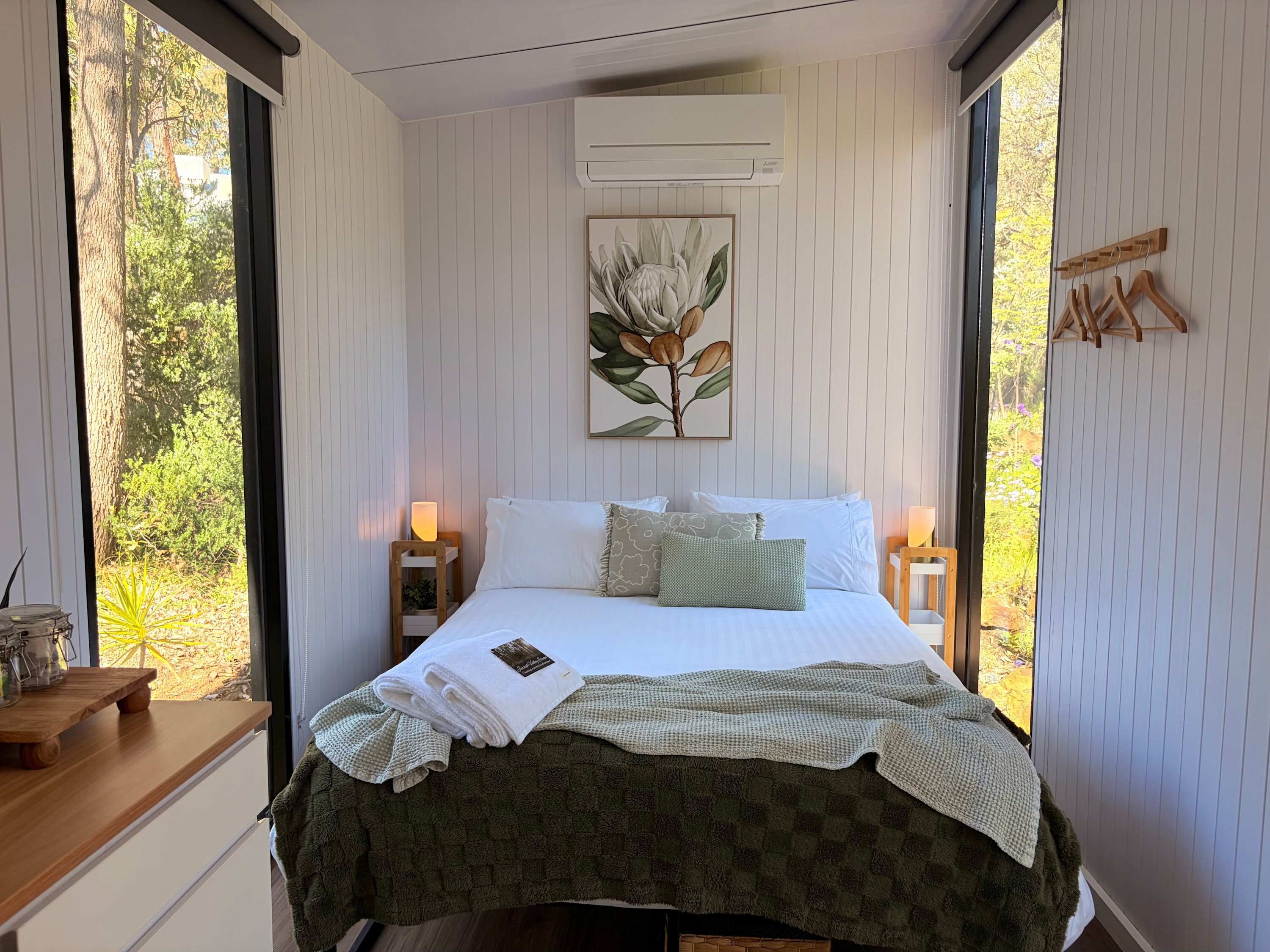 Une chambre à coucher avec un lit, des lampes de chevet, un climatiseur fixé au mur et une fenêtre donnant sur des arbres.