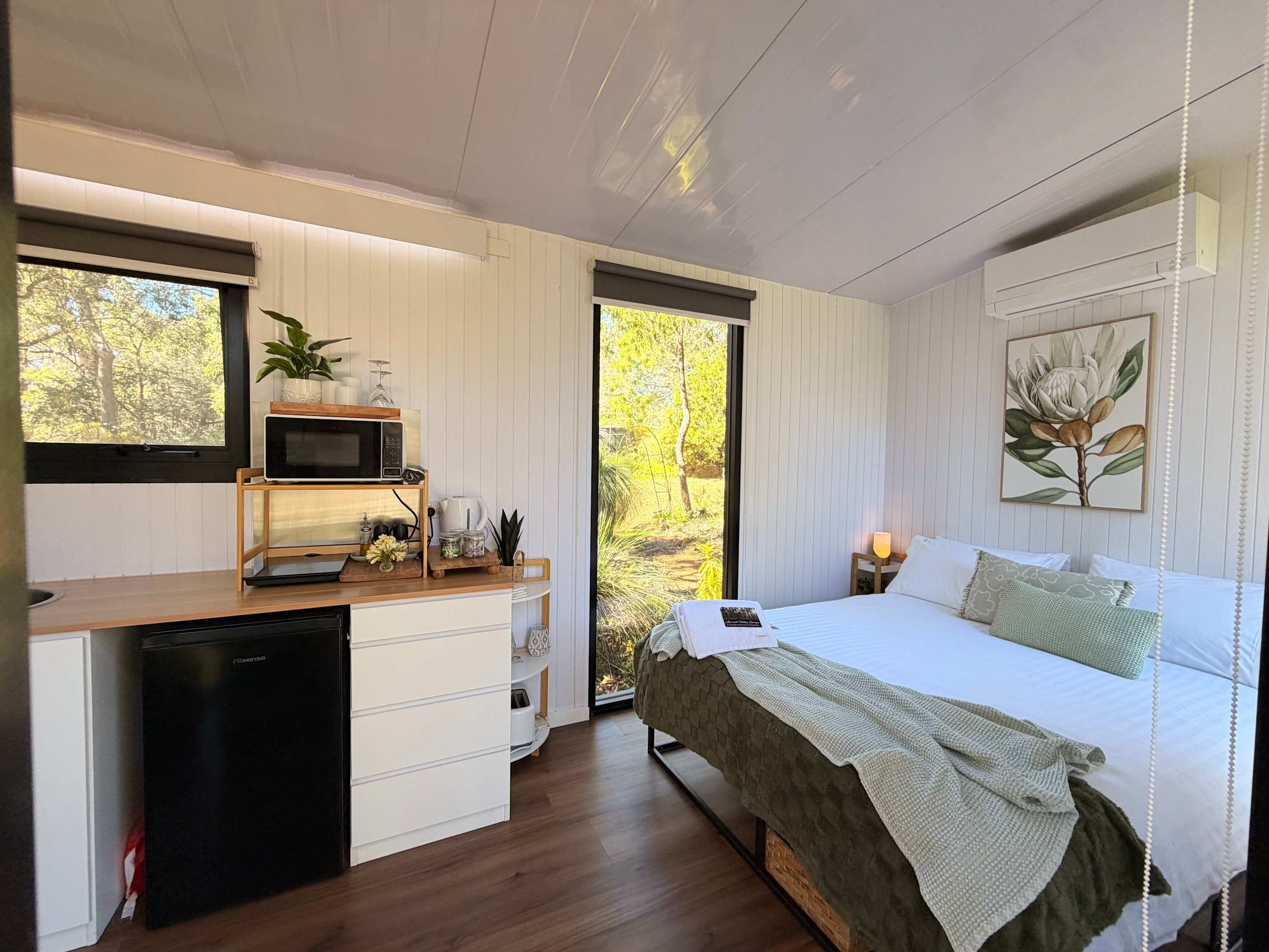 Een slaapkamer met een bed, nachtkastje en een raam met uitzicht op bomen.