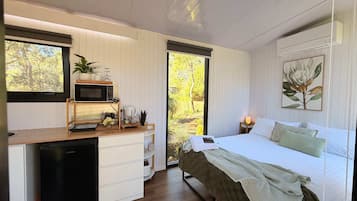 Een slaapkamer met een bed, nachtkastje en een raam met uitzicht op bomen.