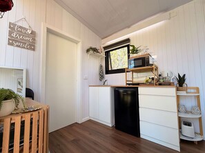Een compacte keuken met een zwarte vaatwasser, een magnetron en een houten plank met diverse spullen.