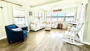 A living room with a sectional sofa, a blue armchair, and a rocking chair. There are large windows and a ceiling fan. - Cozy Retreat , steps to the beach, heated pool , gulf views & huge party Deck (Panama City Beach)
