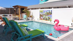 A swimming pool with lounge chairs, a flamingo float, and a mural on the wall. - Cozy Retreat , steps to the beach, heated pool , gulf views & huge party Deck (Panama City Beach)