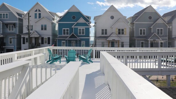 A row of beach houses with a wooden deck and chairs. - Cozy Retreat , steps to the beach, heated pool , gulf views & huge party Deck (Panama City Beach)