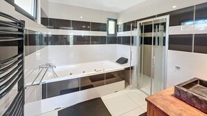 Une salle de bain moderne avec une grande baignoire, une douche à l’italienne avec des parois en verre et un meuble-lavabo en bois.