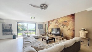 Un salon moderne avec un grand canapé d’angle, une table basse, un téléviseur à écran plat et une fresque représentant une carte du monde.