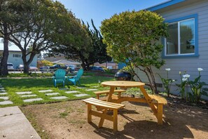 A backyard with a wooden picnic table and chairs, a lawn, and a house in the background.