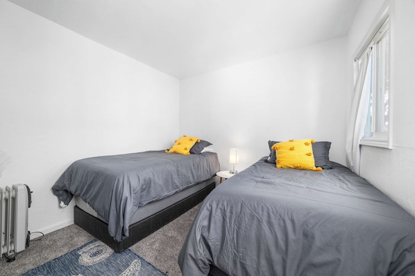 A small, clean room with two beds, a nightstand, and a window.