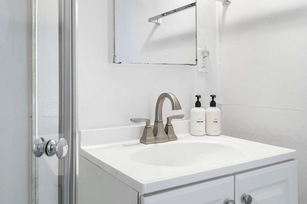 A bathroom with a white sink, a modern faucet, and two bottles of hand soap and lotion.