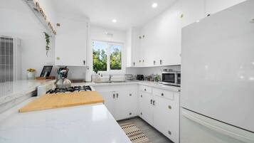 Een moderne keuken met witte kastjes, een gasfornuis, een magnetron en een koelkast.