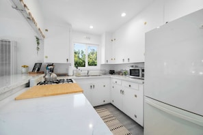 A modern kitchen with white cabinetry, a gas stove, a microwave, and a refrigerator.