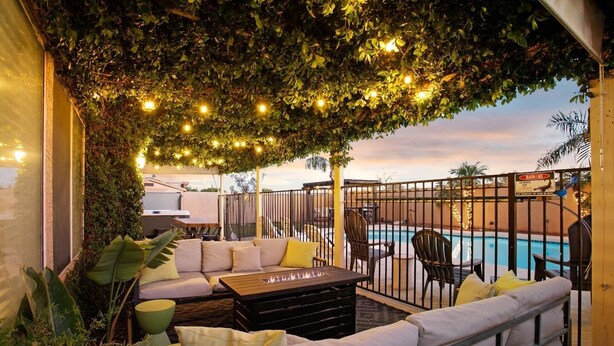 Un área de estar al aire libre con piscina, cubierta por un dosel de follaje y luces colgantes.