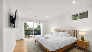 A bedroom with a wooden bed, a nightstand, a TV mounted on the wall, and a view of a balcony with a wooden deck. - 2 Bedroom Aptos Home With Ocean View! (Aptos)