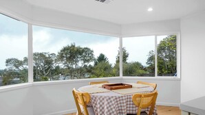 A dining area with a table set for two, large windows, and a view of trees and a body of water. - 2 Bedroom Aptos Home With Ocean View! (Aptos)