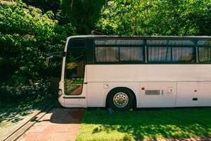 Ein stehender Bus auf einem befestigten Weg, im Hintergrund eine Steinmauer und üppiges Grün.