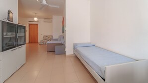 Une chambre à coucher de taille modeste, comprenant un lit simple, un petit canapé, une armoire et un ventilateur de plafond.