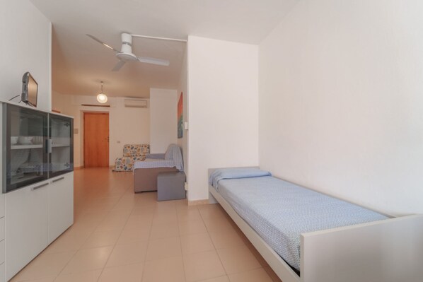 A compact bedroom with a single bed, a small sofa, a cabinet, and a ceiling fan.