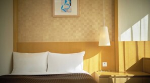 Hotellihuone, jossa on sänky, yöpöytä, lamppu ja seinälle ripustettu taideteos.