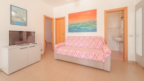 A living room with a sofa, a TV, and a painting of a sunset. - APPARTAMENTI GLI ORIZZONTI - ORIZZONTI N QUADRI 1 (Marina di Campo)