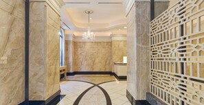 Um corredor com piso de mármore e um design geométrico, um candelabro e um painel decorativo.