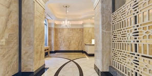 A marble-floored hallway with a geometric floor design, a chandelier, and a decorative screen.